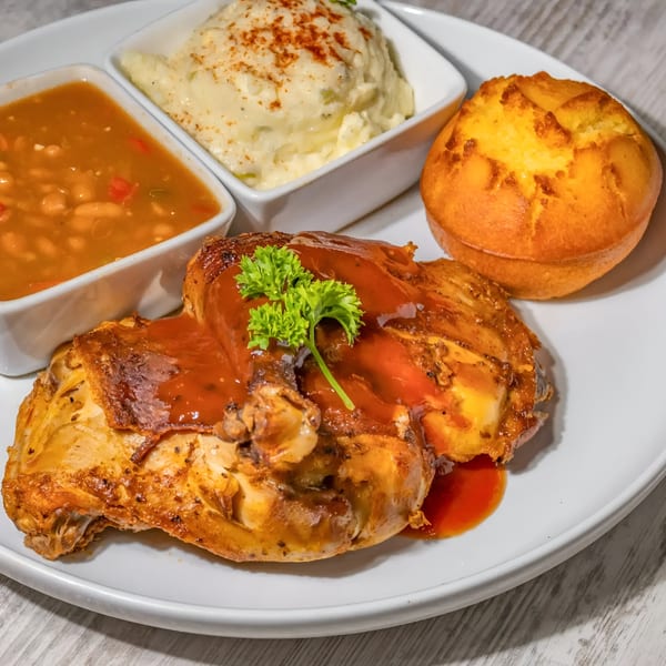 Southern grilled chicken with BBQ sauce, baked beans, mashed potatoes, and a cornbread muffin.