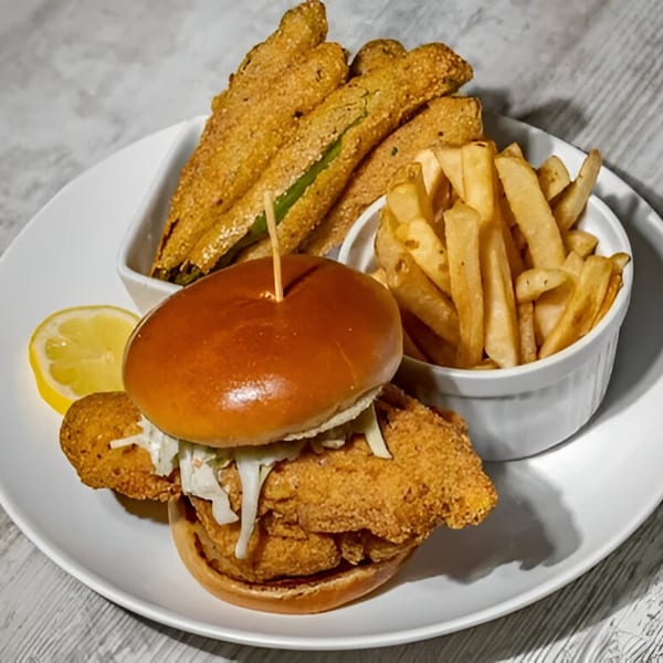 Southern fried fish sandwich with coleslaw, a side of fries, and fried okra on a white plate.