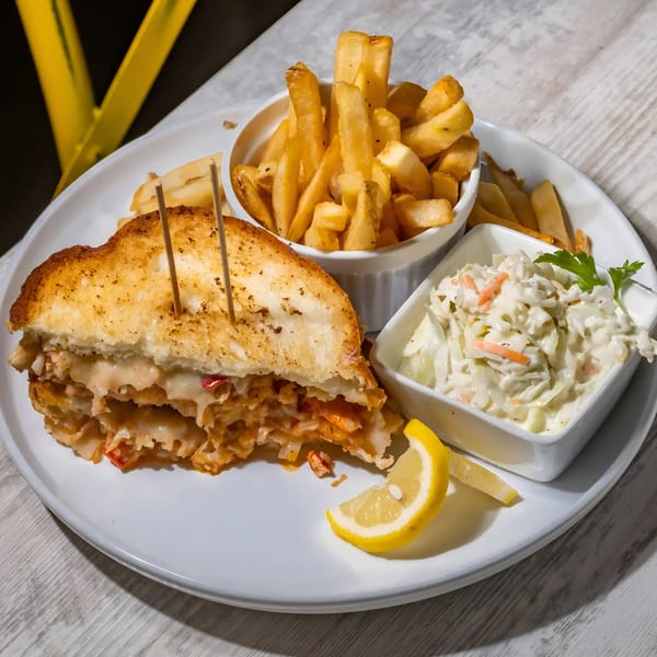 A Southern Grill sandwich with melted cheese, fries, coleslaw, and a lemon wedge on a white plate.