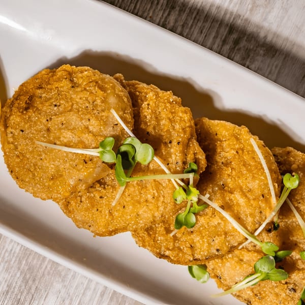 Golden-fried green tomatoes, garnished with fresh microgreens, on a white rectangular plate.