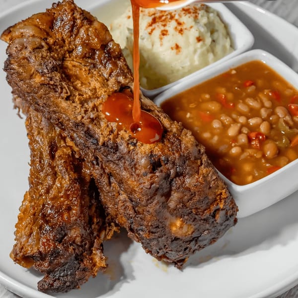 Two large pieces of southern-style meat, possibly ribs, with sauce being poured over them.